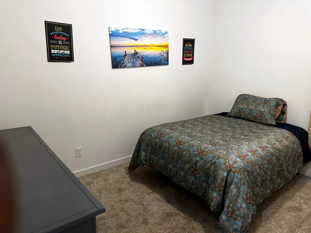 Comfortable youth bedroom with a floral bedspread and a sunset canvas on the wall